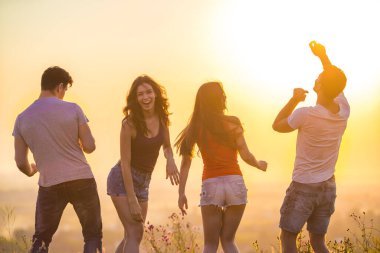 Güneşli arka planda dans eden dört kişi