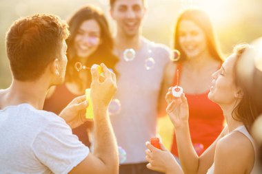 İnsanlar güneşli arka planda baloncuklar üflüyor.