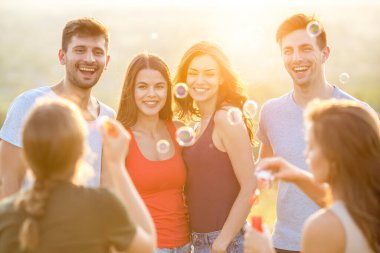 Mutlu insanlar güneşli arka planda baloncuklar üflüyor.