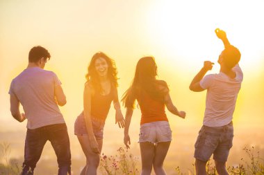 Parlak günbatımının arka planında dans eden dört kişi