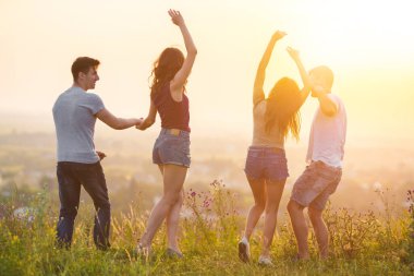 Güneşin arka planında dans eden dört kişi