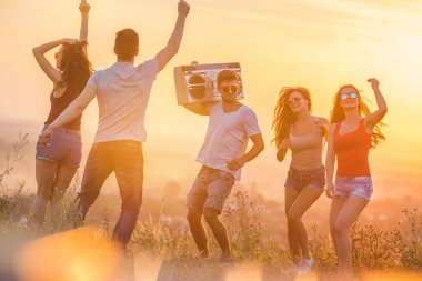 Beş mutlu arkadaş günbatımının arka planında bir teyple dans ediyor.