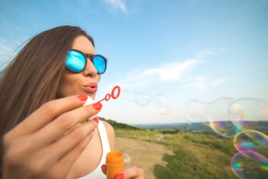 Çekici kadın mavi gökyüzünün arka planına baloncuklar üflüyor.