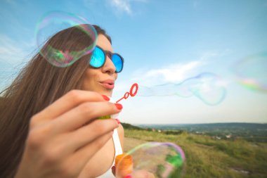 Çekici kadın mavi gökyüzünün arka planına baloncuklar üflüyor.