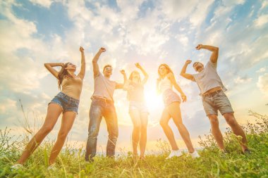 Güneşli arka planda çimenlerde dans eden beş arkadaş.