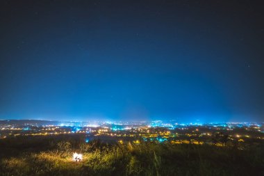 Bir şehrin arka planındaki şenlik ateşi ve yıldızlı bir gökyüzü. Gece vakti.