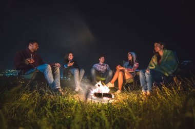 Beş kişi şenlik ateşinin yanında dinleniyor. Akşam vakti.