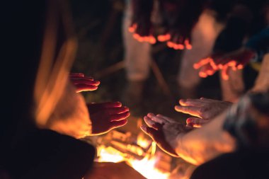 İnsanlar şenlik ateşinin yanında ellerini ısıtıyorlar. Gece vakti.