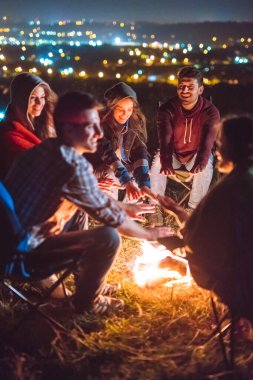 Şenlik ateşinin yanında elini ısıtan mutlu insanlar. Akşam vakti.