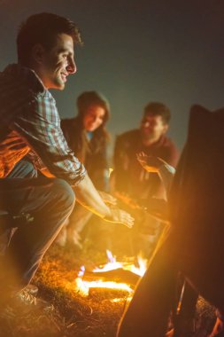 İnsanlar şenlik ateşinin üstünde ellerini ısıtıyorlar. Akşam vakti.