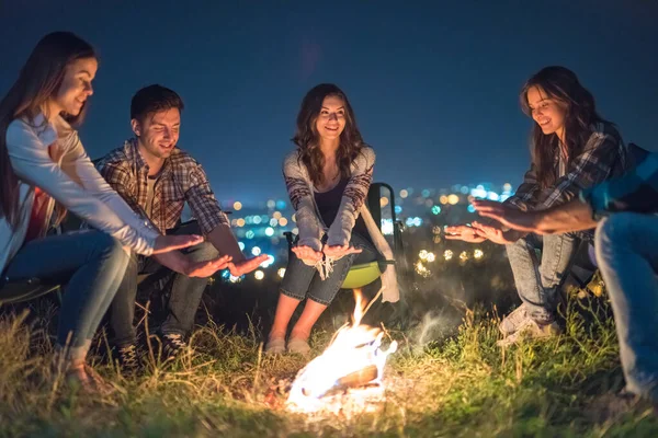 The young people warming near a bonfire on a city lights background. night time