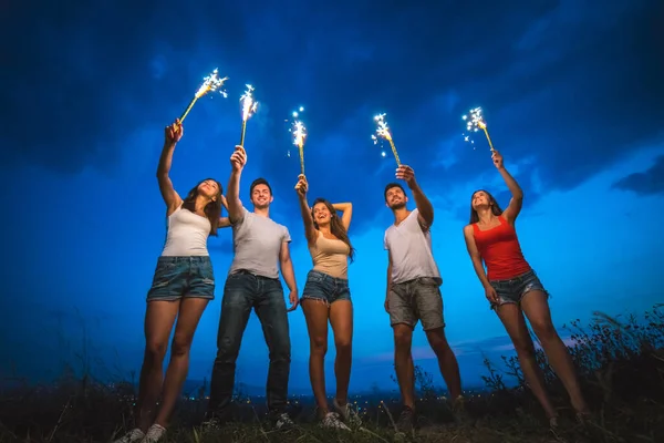 stock image The happy friends hold firework sticks. evening night time