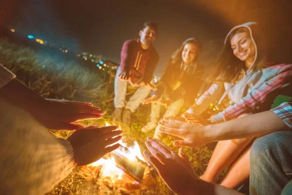 The happy people warming hands near a bonfire. evening night time