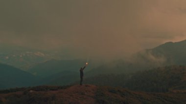 Dağın tepesinde elinde bir ateş sopasıyla duran erkek.