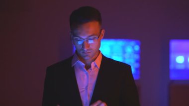 Gözlüklü adam karanlık odada tabletle çalışıyor.