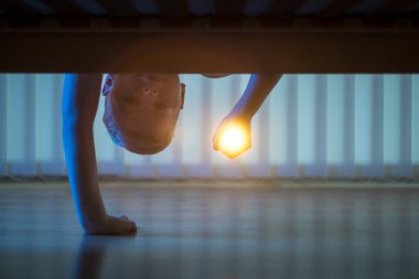 Yatağın altında el feneri olan çocuk. Gece vakti.