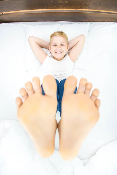 The boy relax on the bed and show feet. view from above