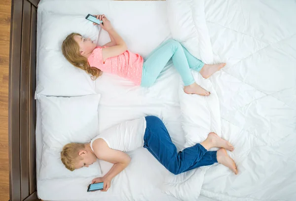 The boy and girl with phones lay on the bed. view from above