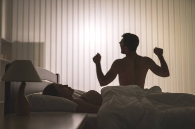 Yatakta bir kadının yanında egzersiz yapan adam.