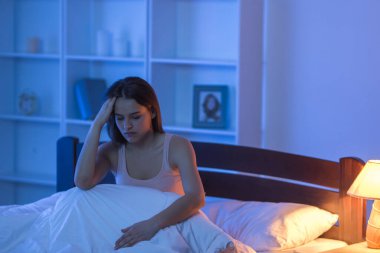 Başı ağrıyan kadın yatakta oturuyor. Gece vakti.