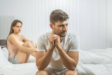 Endişeli adam yatakta kadının yanında oturuyor.