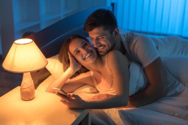 Gülümseyen aşıklar yatak odasında telefon ediyorlar. Gece vakti.