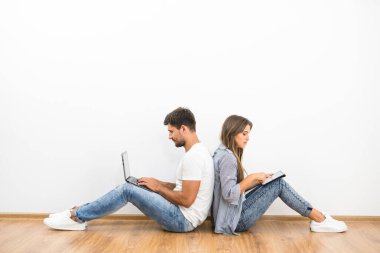 Çift boş duvarın yanında dizüstü bilgisayar ve tabletle oturuyor.