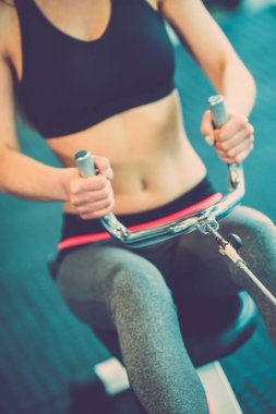 Atletik kadın eğitim aletinin kolunu çekiyor.