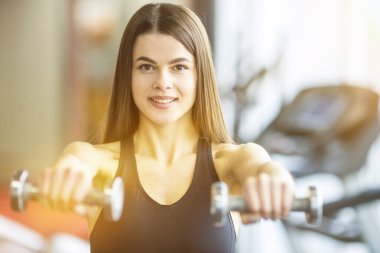 Genç kadın spor kulübünde dambılları tutuyor.