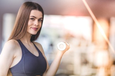 Spor salonunda dambıllarla egzersiz yapan mutlu kadın.