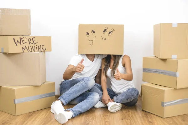 The man and woman sit on the floor with a carton box on the heads and gesture