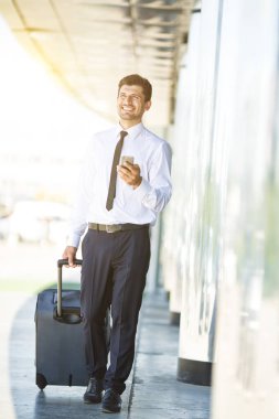Mutlu iş adamı telefonu ve binanın yanında bir bavulla yürüyor.