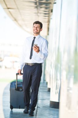 İş adamı telefon eder ve binanın yanında bir bavulla yürür.