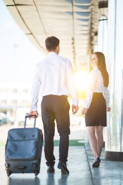 İş adamı ve kadın, modern binanın yakınında bir bavulla yürüyorlar.