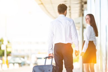 İş adamı ve kadın binanın yanında bir bavulla yürüyorlar.