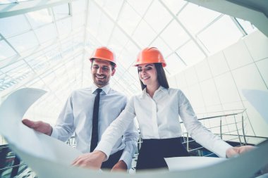 Miğferli mutlu adam ve kadın proje planını binanın içinde tutuyorlar.