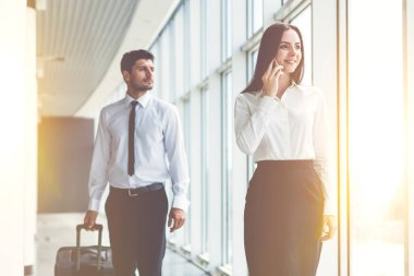 İş kadını, elinde bavul olan adamın yanındaki telefonu arıyor.