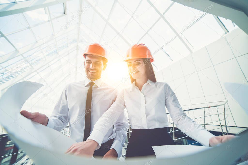 The man and woman in a helmets hold the project plan in the building