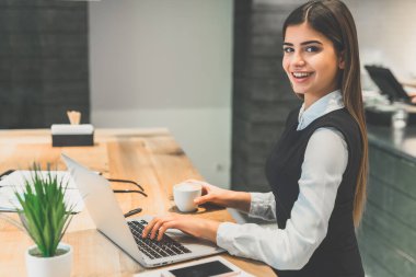 Kahve içip dizüstü bilgisayarla çalışan mutlu kadın.