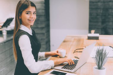 Kahve içip dizüstü bilgisayarla çalışan mutlu iş kadını.