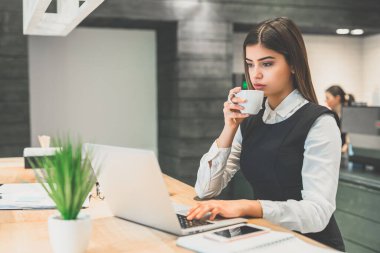 İş kadını kahve içiyor ve dizüstü bilgisayarla çalışıyor.