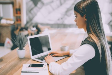 Kadın masada modern bir dizüstü bilgisayarla çalışıyor.