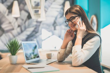 Kulaklıklı mutlu iş kadını masada modern laptopuyla oturuyor.
