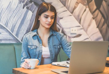 Kahve içen ve bilgisayarla çalışan kadın.