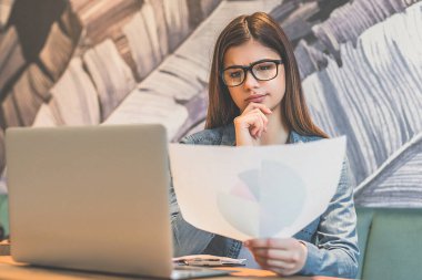 Masada elinde gazete tutan gözlüklü ciddi kadın.