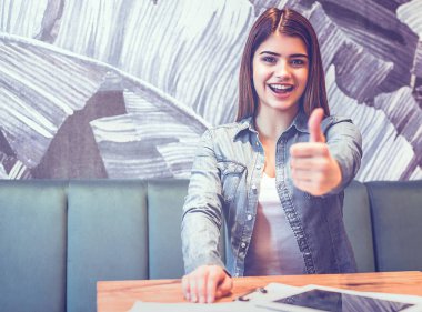 Kafedeki masada el kol hareketi yapan mutlu kadın.