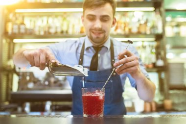 Barmen barın üstünde buz olan kırmızı bir kokteyl yapıyor.