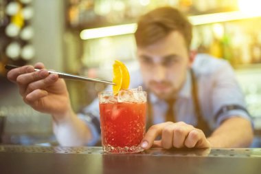 Barmen barın üstünde portakalla kırmızı kokteyl yapıyor.