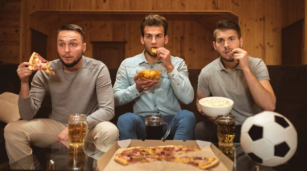 The three friends watch a football and eat