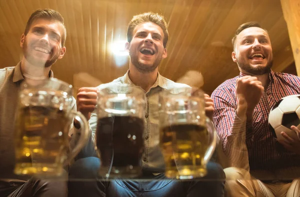 The three happy friends with a beer watch a football